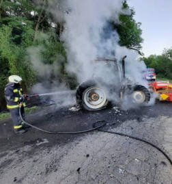 A képen egy tűzoltó vízsugárral oltja a traktortüzet.